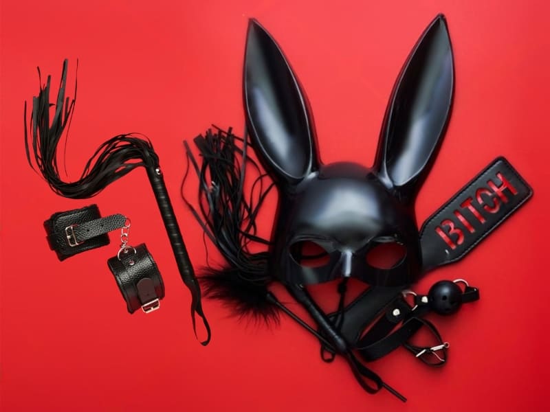 Plusieurs accessoires utilisés pour pratiquer le BDSM (menottes en cuir, fouet, muselière, plumeau, masque de lapin en cuir...).